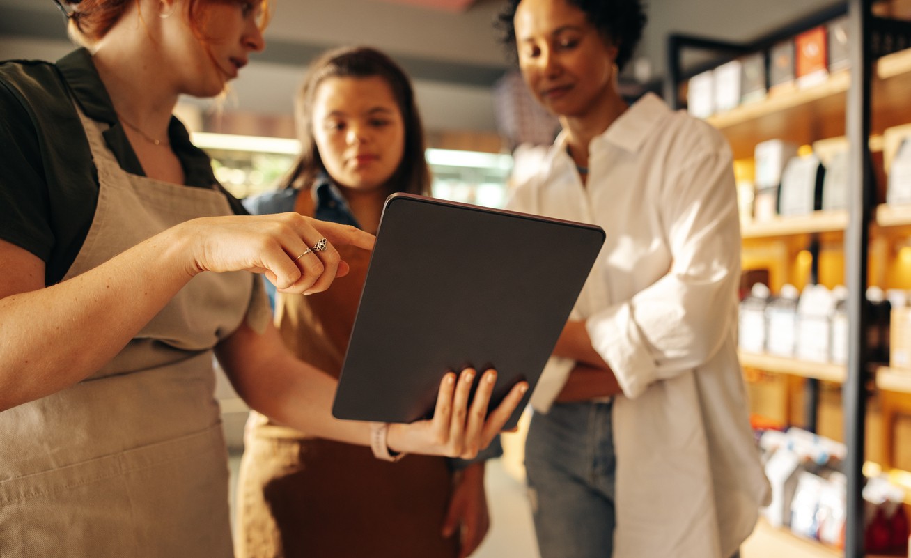 Grocery store manager using a digital tablet while having a discussion with her employees in a staff meeting. Group of diverse women working together in an all-female small business.