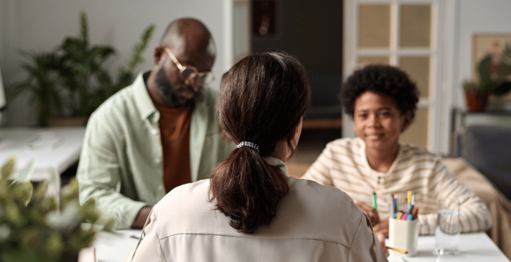 A behaviour consultant sits across from a parent and child in a bright, welcoming office setting. The consultant listens attentively while the child smiles and engages with colorful stationery on the table. This image represents the collaborative and supportive nature of the Behaviour Consulting program at the SAAAC Autism Centre, which helps families navigate challenging behaviours through individualized strategies rooted in ABA principles.