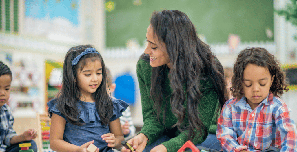 A therapist interacts warmly with two young children as they engage in a play-based learning activity in a classroom setting. The children sit side by side, practicing social and communication skills through guided interaction. This image represents the Dyad ABA Therapy program at the SAAAC Autism Centre, which supports development through structured peer-based learning and individualized behaviour strategies.